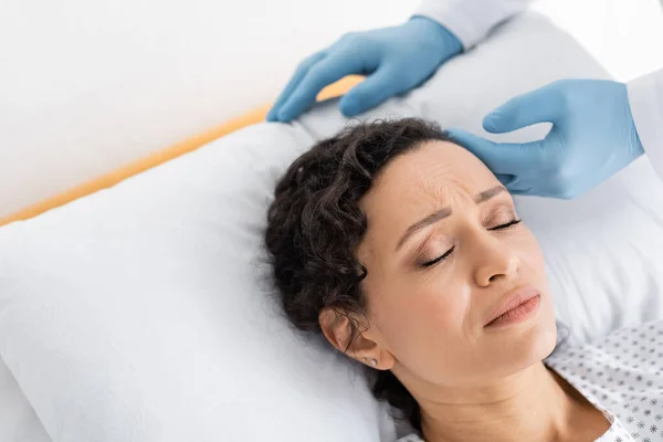 Medico in guanti di lattice toccare la testa di una donna afroamericana malata sdraiata ad occhi chiusi — Foto stock