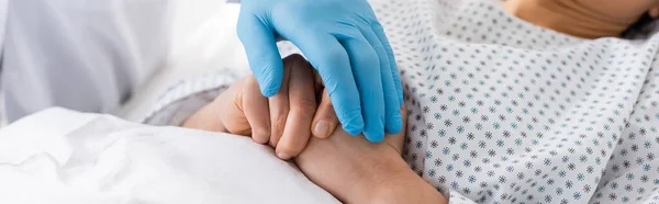 Ausgeschnittene Ansicht eines Arztes im Latexhandschuh, der Hände einer kranken Frau berührt, Banner — Stockfoto