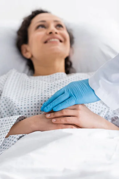 Médecin en gant de latex toucher les mains d'une femme afro-américaine souriante sur fond flou — Photo de stock