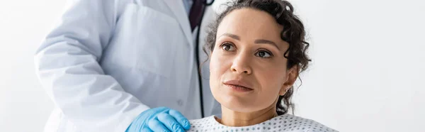 Médico em luva de látex tocando ombro de mulher afro-americana doente, bandeira — Fotografia de Stock