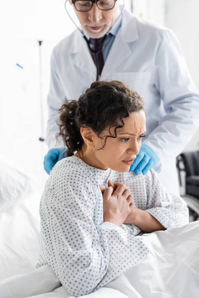 Kranke Afroamerikanerin hustet, während Arzt sie mit Stethoskop auf verschwommenem Hintergrund untersucht — Stockfoto
