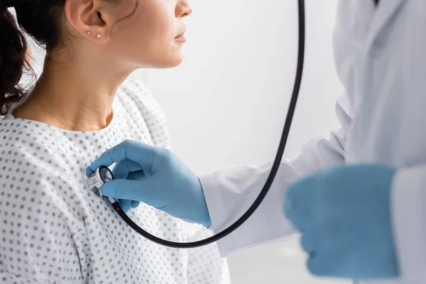 Vista recortada del médico en guantes de látex examinando mujer afroamericana con estetoscopio - foto de stock