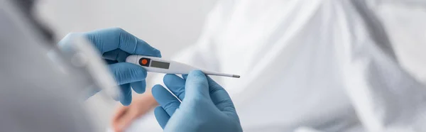 Vista recortada del médico en guantes de látex con termómetro, pancarta - foto de stock