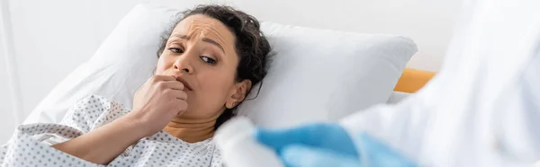 Besorgte Afroamerikanerin liegt im Krankenhausbett neben Arzt mit Medikamenten im verschwommenen Vordergrund, Transparent — Stockfoto