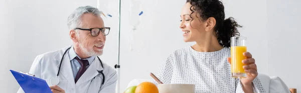 Happy african american woman having breakfast near smiling doctor in hospital, banner — Stock Photo