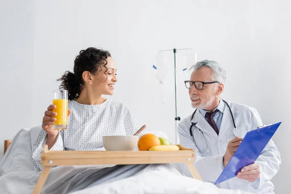 Smiling doctor showing prescription to african american woman during breakfast in clinic — Stock Photo