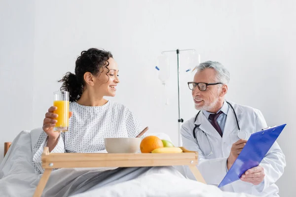 Medico sorridente che mostra prescrizione alla donna afro-americana durante la colazione in clinica — Foto stock