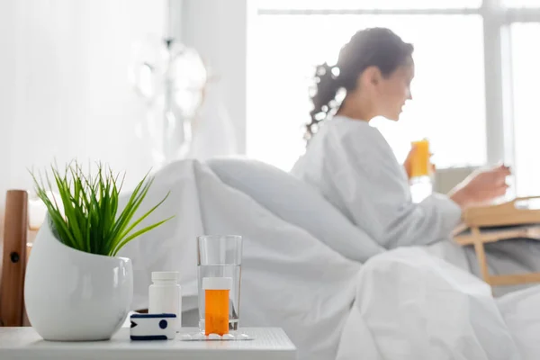Oxímetro de pulso, medicamentos e planta verde perto de mulher afro-americana tomando café da manhã em fundo turvo — Fotografia de Stock