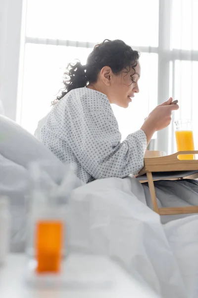 Mujer afroamericana desayunando cerca de un vaso de jugo de naranja en la clínica, borrosa en primer plano - foto de stock