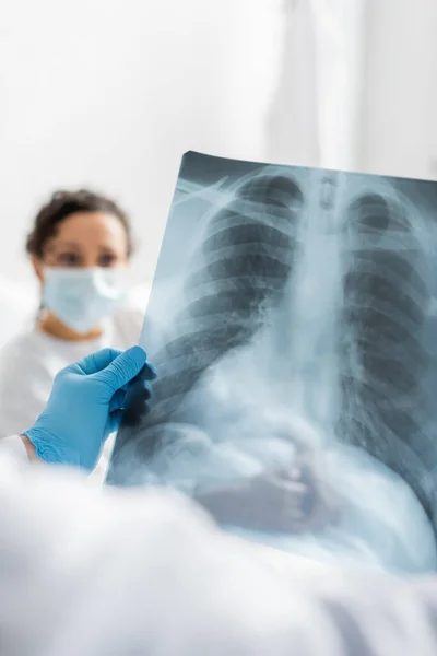 Radiologist in latex glove holding lungs x-ray near african american woman in medical mask on blurred background — Stock Photo