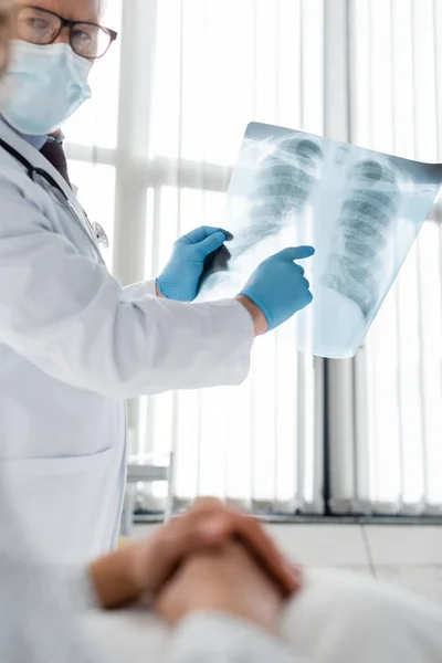 Radiologe in medizinischer Maske zeigt auf Lungen-Röntgenbild nahe Afroamerikanerin auf verschwommenem Vordergrund — Stockfoto