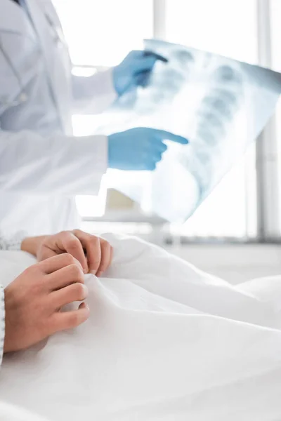 Обрізаний вид радіолога в латексних рукавичках, що вказує на рентгенівський промінь легень біля пацієнта в лікарні, розмитий фон — стокове фото