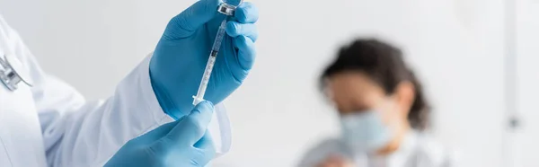 Cropped view of doctor in latex gloves holding syringe with vaccine near african american woman on blurred background, banner — Stock Photo