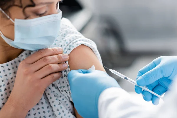 Vue partielle du médecin en gants de latex faisant la vaccination de la femme afro-américaine en masque médical — Photo de stock