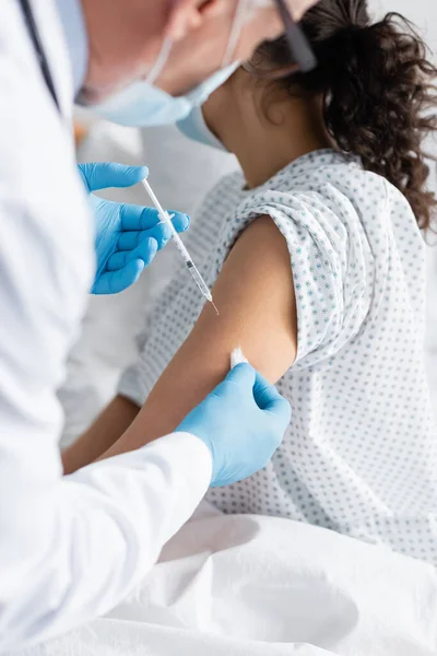 Vue recadrée du médecin en gants de latex faisant la vaccination de la femme afro-américaine, premier plan flou — Photo de stock