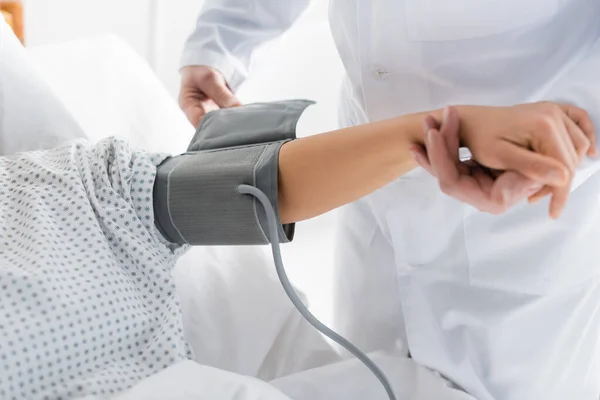 Vista recortada del médico poniendo manguito tonómetro en la mano de la mujer - foto de stock