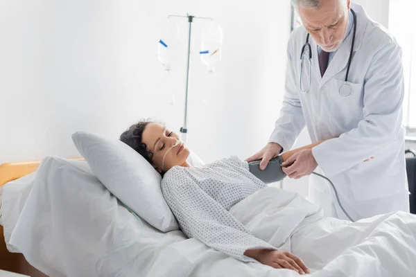 Médico medir a pressão arterial da mulher afro-americana deitada na cama do hospital — Fotografia de Stock