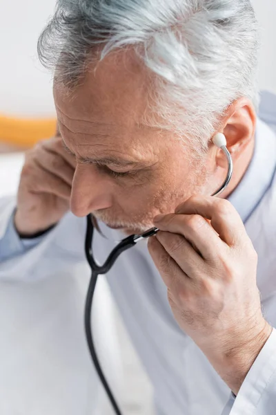 Vue grand angle du médecin mature ajustant stéthoscope à l'hôpital — Photo de stock