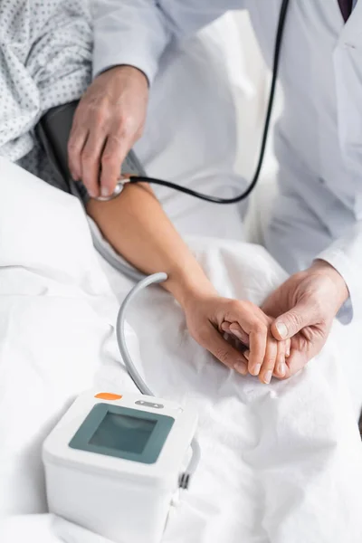 Vista recortada del médico que mide la presión arterial de la mujer en el hospital - foto de stock