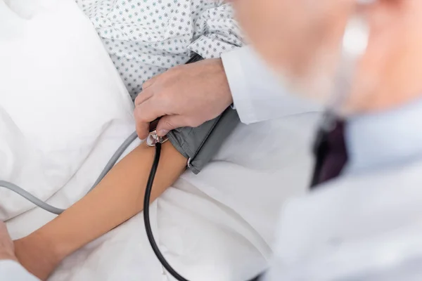 Vista parziale del medico con tonometro sulla donna in ospedale, primo piano sfocato — Foto stock