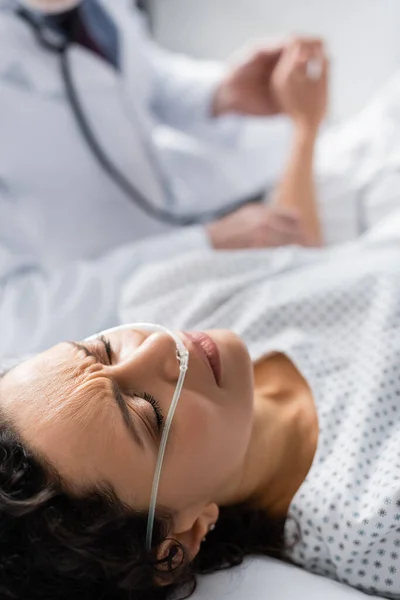 Mulher afro-americana doente com cânula nasal que sofre de dor perto do médico em fundo turvo — Fotografia de Stock