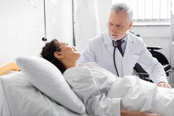 Mature doctor examining african american women with stethoscope in clinic — Stock Photo