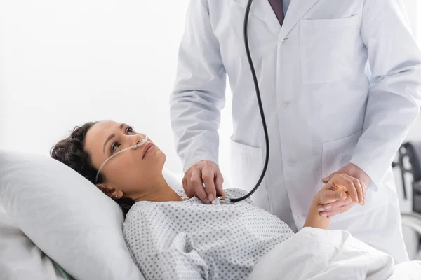 Medico che tiene per mano una donna afroamericana malata mentre la esamina con stetoscopio — Foto stock
