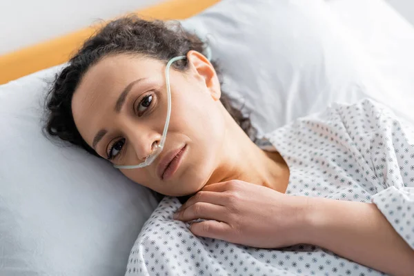 Над головой вид больной африканской женщины с носовым канюлем, смотрящей в камеру, лежащей на больничной койке — стоковое фото