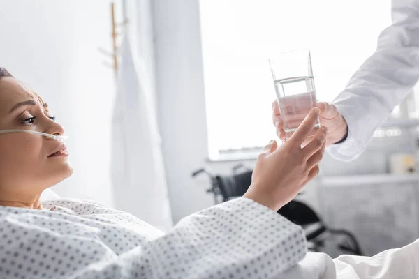 Diseased african american woman taking glass of water from doctor in clinic — Stock Photo