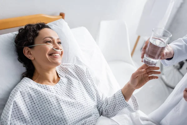 Donna afro-americana sorridente che prende un bicchiere d'acqua dal medico in ospedale — Foto stock