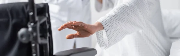 Teilbild einer Frau mit ausgestreckter Hand in der Nähe des Rollstuhls auf verschwommenem Vordergrund, Banner — Stockfoto