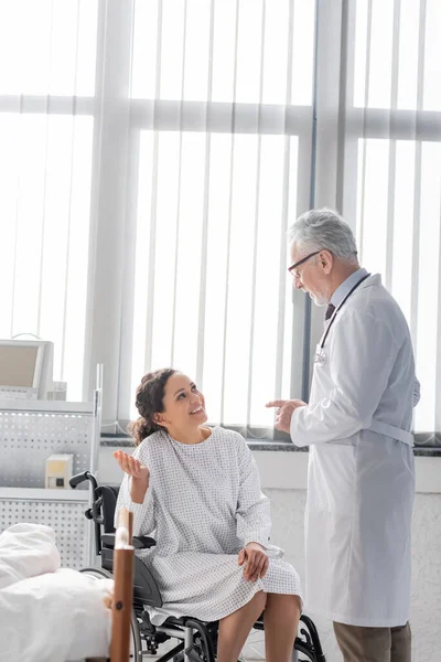 Cheerful african american woman in wheelchair talking to mature doctor in hospital — Stock Photo