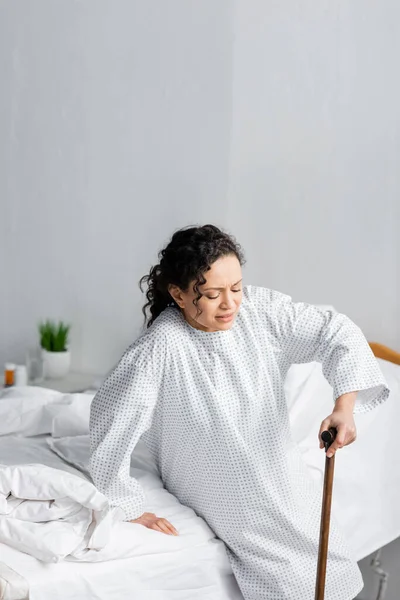African american woman leaning on walking stick while getting up from hospital bed — Stock Photo