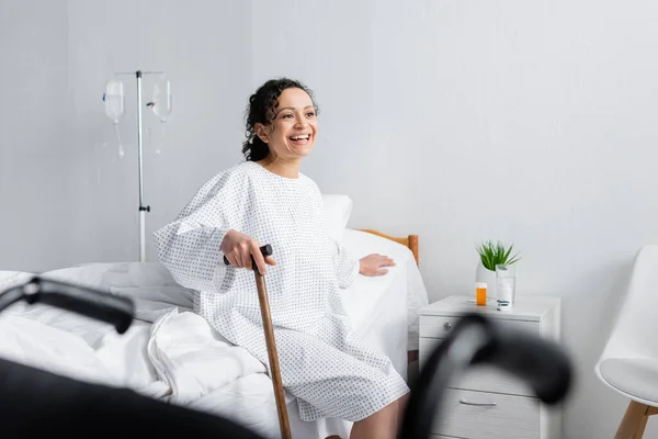 Mulher americana africana feliz com bengala sentada na cama do hospital, foreground borrado — Fotografia de Stock