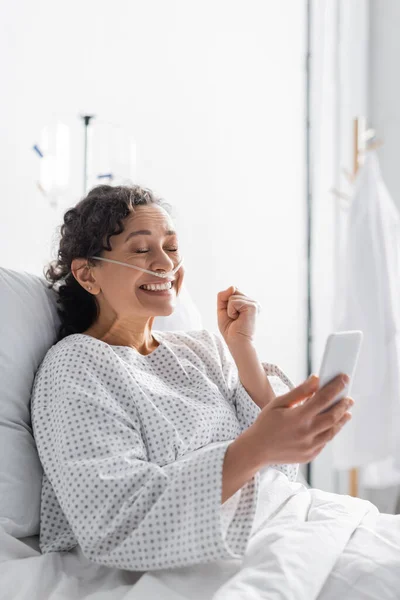 Aufgeregte Afroamerikanerin zeigt Siegergeste, während sie ihr Handy in der Klinik hält — Stockfoto
