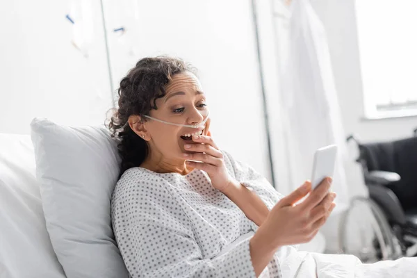 Mulher afro-americana surpreendido cobrindo boca enquanto olha para o celular na clínica — Fotografia de Stock