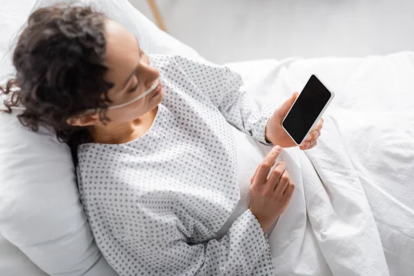 Vista aerea della donna afro-americana malata che tiene lo smartphone con schermo bianco in clinica — Foto stock