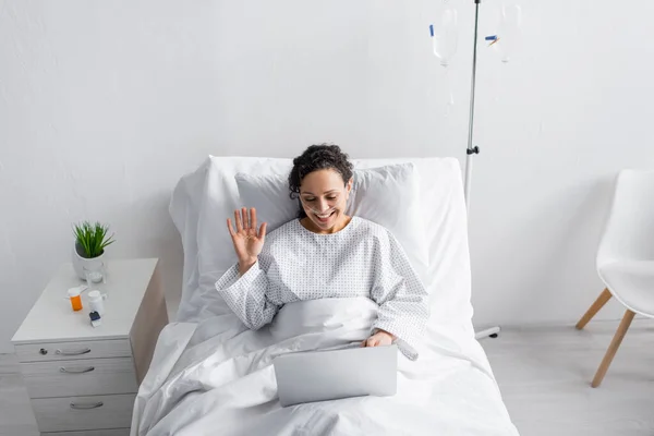 Vista de ángulo alto de la mujer afroamericana agitando la mano durante la videollamada en el ordenador portátil en la clínica — Stock Photo