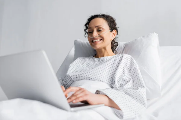 Femme afro-américaine gaie tapant sur ordinateur portable à l'hôpital sur le premier plan flou — Photo de stock
