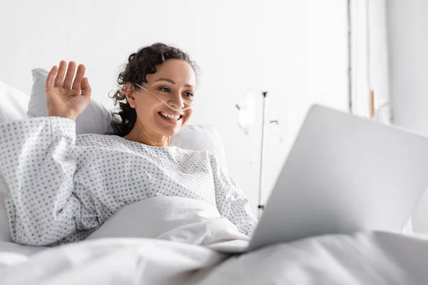 Femme afro-américaine agitant la main pendant le chat vidéo sur ordinateur portable à l'hôpital au premier plan flou — Photo de stock