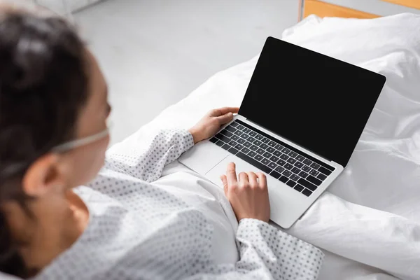 African american woman near laptop with blank screen in hospital, blurred foreground — Stock Photo