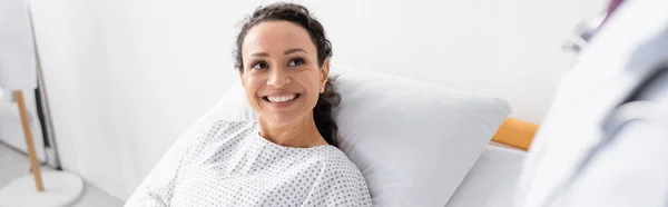 Joyeuse femme afro-américaine souriant près du médecin au premier plan flou, bannière — Photo de stock