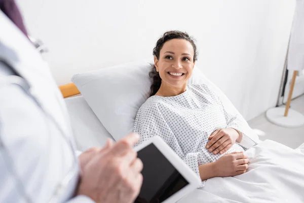 Cheerful african american woman looking at doctor with digital tablet on blurred foreground — Stock Photo