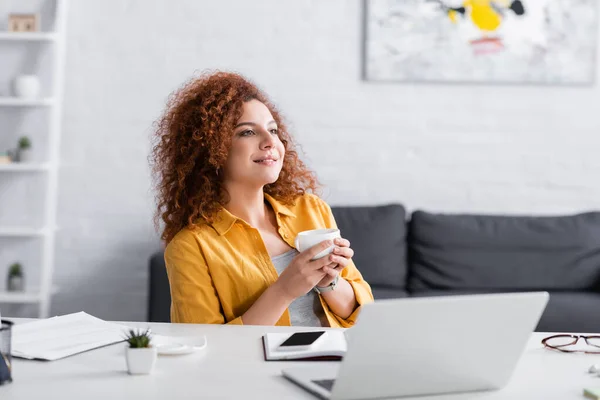 Muito freelancer sentado com xícara de café perto de laptop em casa — Fotografia de Stock