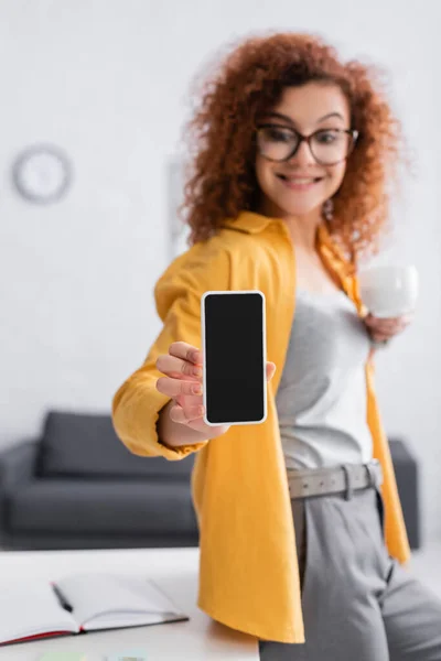 Fröhliche Freiberuflerin zeigt Handy mit leerem Bildschirm, verschwommenem Hintergrund — Stockfoto