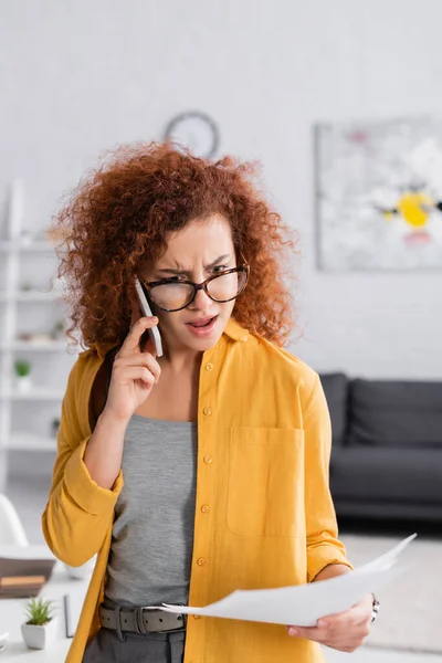 Displeased freelancer talking on mobile phone while holding documents — Stock Photo