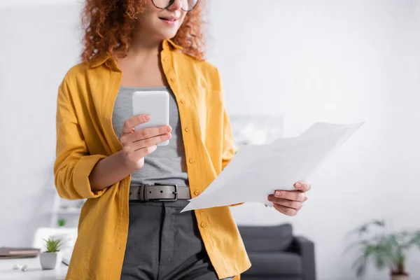 Vista recortada del joven freelancer sosteniendo documentos y taza de café - foto de stock