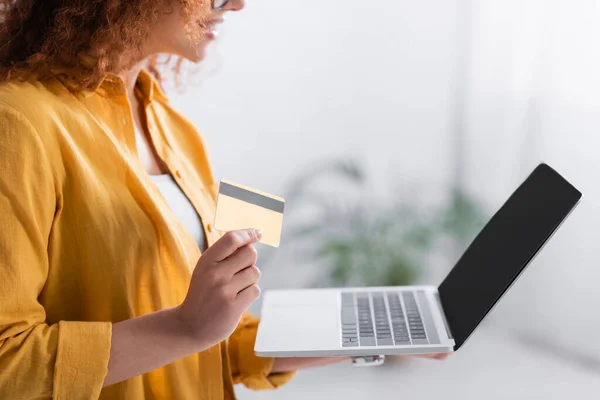 Vue recadrée de la femme tenant la carte de crédit près d'un ordinateur portable avec écran blanc — Photo de stock