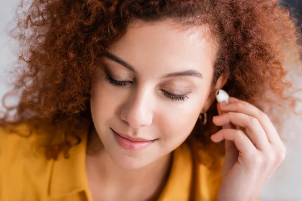 Mulher bonita com cabelo ondulado segurando fone de ouvido sem fio — Fotografia de Stock