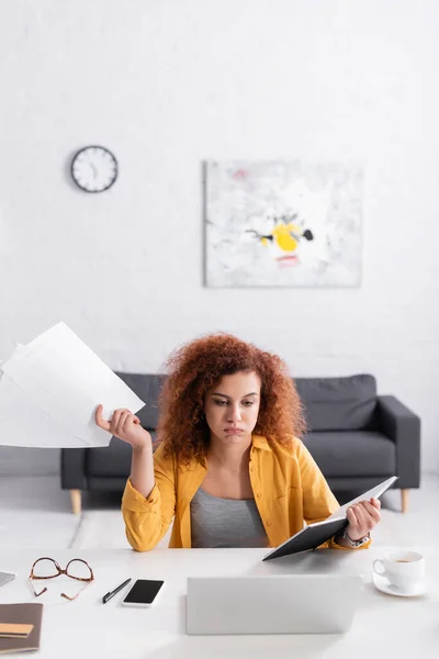 Freelance épuisé tenant des documents et un carnet tout en étant assis près d'un ordinateur portable — Photo de stock